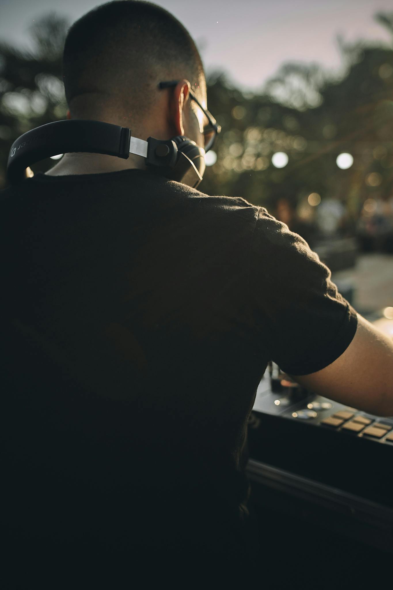 Back view of a DJ wearing headphones, working at an outdoor event during dusk.