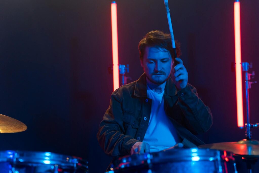 Musician playing drums in neon-lit studio with intense focus.